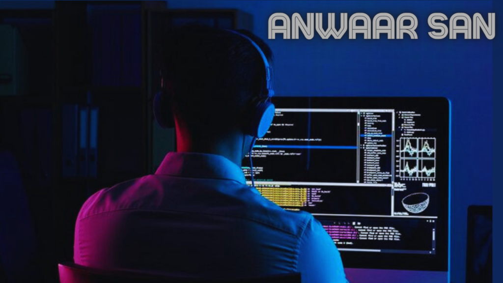 This image depicts a person working on a computer in a dark room. The person is wearing headphones and appears to be focused on the computer screen. Multiple windows are open on the computer screen, including texts and graphs, indicating that the person is multitasking or working on a complex task. The text “ANWAAR SAN” is prominently displayed at the top of the screen in white letters against a black background.